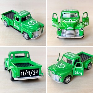 May include: Green toy pickup truck with white lettering that says "Ring Bearer" and "Johnny". The truck has two white rings on the hood and a black sign on the back that says "11/11/24".