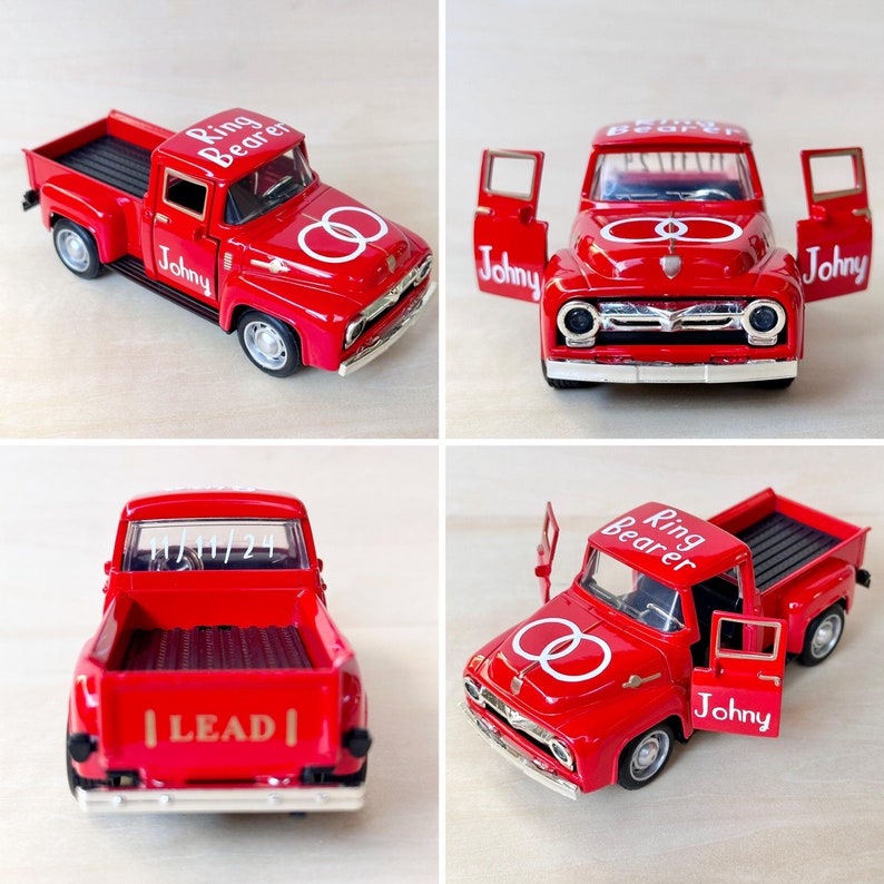 May include: Four red toy pickup trucks with white lettering. The trucks have the words "Ring Bearer" and "Johny" on them. One truck has the words "Lead" on the back. The trucks have white rings on the sides.