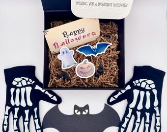 May include: A Halloween-themed gift box with a black lid, filled with decorative items. Includes a card that says "Wishing you a wonderful Halloween", a "Happy Halloween" card, stickers, a bat, and skeleton gloves.