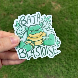 May include: A green and yellow sticker with the text "BAJA BLASTOISE". The sticker features a cartoon turtle character holding a drink and a taco, with green spray bottles in the background.