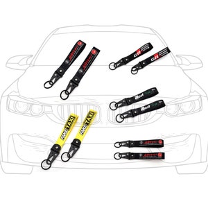 Peut inclure: Un ensemble de six porte-clés différents avec des designs et des couleurs variés. Les porte-clés sont dotés de lanières noires avec du texte et des logos de différentes couleurs, notamment "Fake Taxi", "Drift" et "GR".