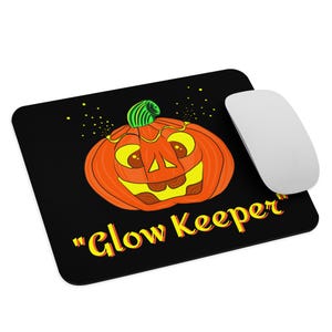 Könnte beinhalten: Schwarzes Mauspad mit einem Cartoon-Kürbis-Design. Der orangefarbene Kürbis hat einen grünen Stiel und gelbe Akzente. Der Text "Glow Keeper" ist gelb. Eine weiße Computermaus befindet sich rechts.