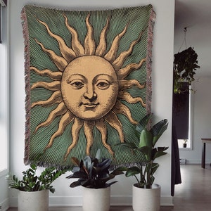 May include: A tapestry featuring a vintage illustration of a sun with a human face, surrounded by rays of light. The background is a deep green with a striped pattern.
