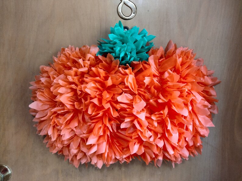 May include: A large orange paper pumpkin decoration with a smaller teal paper flower on top. The pumpkin is made of tissue paper and has a ruffled texture.