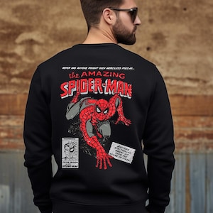 May include: Black sweatshirt with a red and blue comic book style graphic of Spider-Man on the back. The text "NEVER HAS ANYONE FOUGHT SUCH MERCILESS FEAR AS... THE AMAZING SPIDER-MAN" is printed above the graphic.