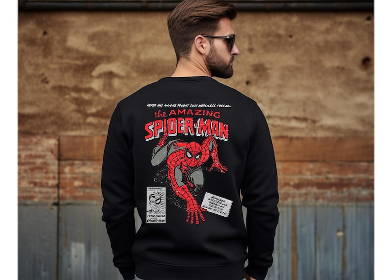 May include: Black sweatshirt with a red and blue comic book style graphic of Spider-Man on the back. The text "NEVER HAS ANYONE FOUGHT SUCH MERCILESS FEAR AS... THE AMAZING SPIDER-MAN" is printed above the graphic.