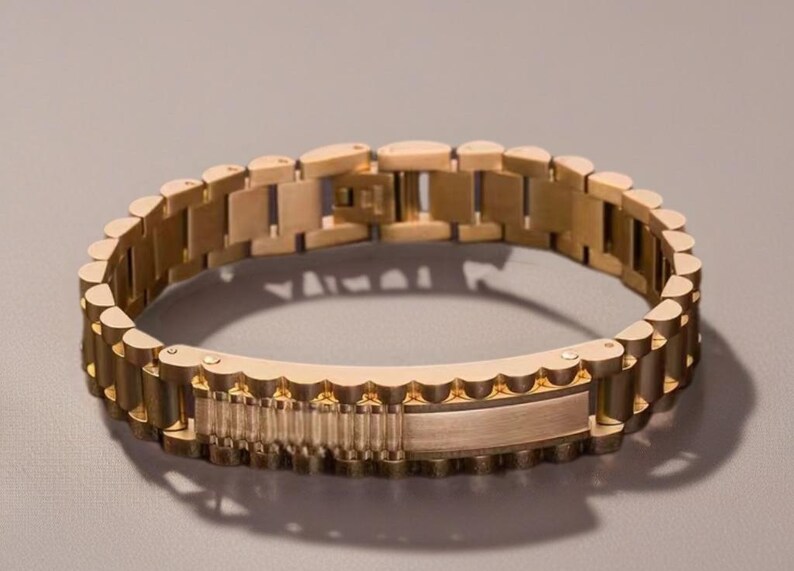 May include: A gold-toned metal bracelet with a textured, interlocking design. The bracelet has a clasp closure.