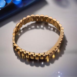 May include: A gold-toned metal bracelet with a link chain design. The bracelet is made of multiple small, connected links.
