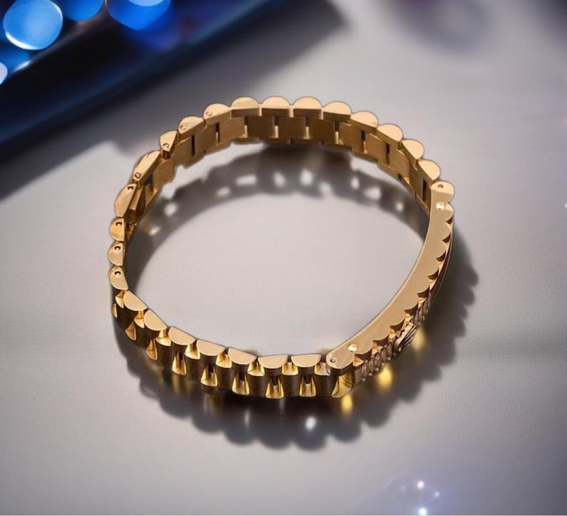 May include: A gold-toned metal bracelet with a link chain design. The bracelet is made of multiple small, connected links.