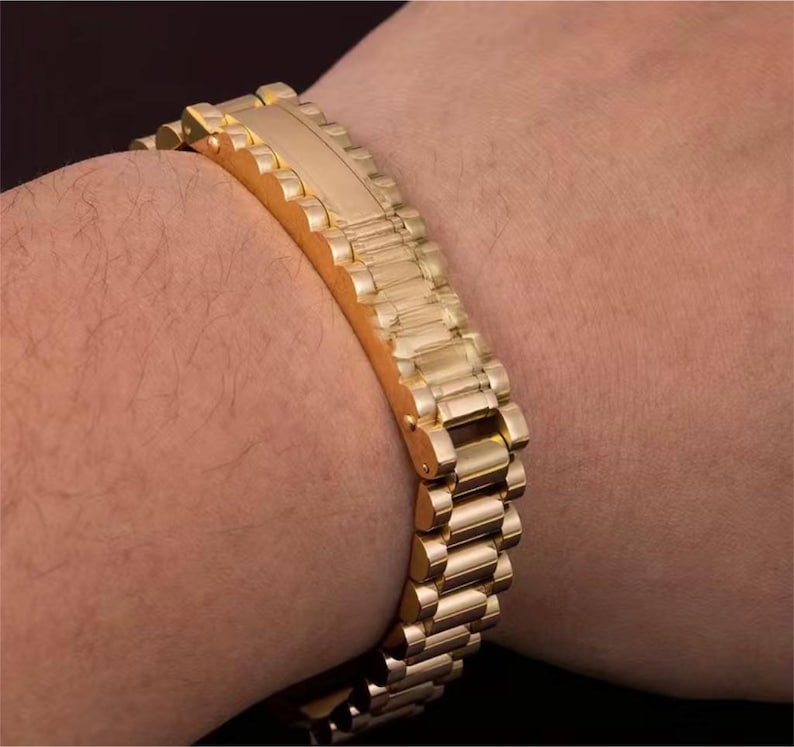 May include: A gold-tone metal watch band with a polished finish. The band is made of individual links that are connected together.