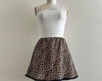 May include: A white tube top and a leopard print skirt on a mannequin. The skirt has a black lace trim at the hem. The skirt features a tan background with dark brown spots.