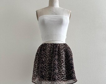 May include: A white tube top and a leopard print mini skirt displayed on a mannequin. The skirt features a brown and black animal print pattern. The outfit is displayed against a plain white background.