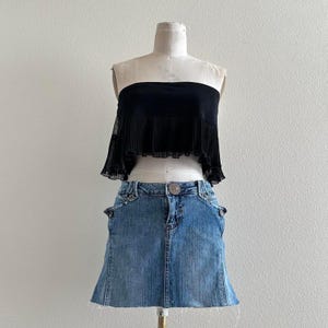 May include: A black strapless top with a pleated, ruffled hemline paired with a light blue denim mini skirt. The skirt has decorative pockets and a button closure. The outfit is displayed on a mannequin.