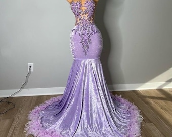 Puede incluir: Un vestido de gala de sirena de terciopelo lavanda con un corpiño de cuentas y un ribete de plumas. El vestido tiene un escote de corazón y una silueta ajustada.