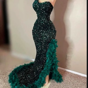May include: A dark green sequined mermaid-style gown with a one-shoulder neckline and a feather trim along the side.