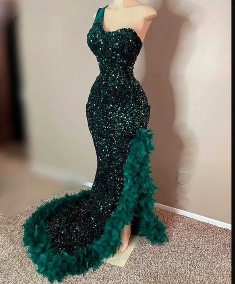 May include: A dark green sequined mermaid-style gown with a one-shoulder neckline and a feather trim along the side.