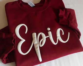 以下が含まれることがあります： ワインレッドのトレーナーに、白い筆記体で「Epic」と書いてあります。
