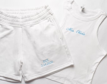 May include: A white tank top and matching shorts set. The tank top has the embroidered text "Mrs. Olivia" in light blue. The shorts have the embroidered text "EST. 2.14.2026" in light blue.