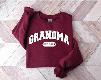 Może przedstawiać: Bordowy sweter z białym napisem "Grandma Est. 2025".