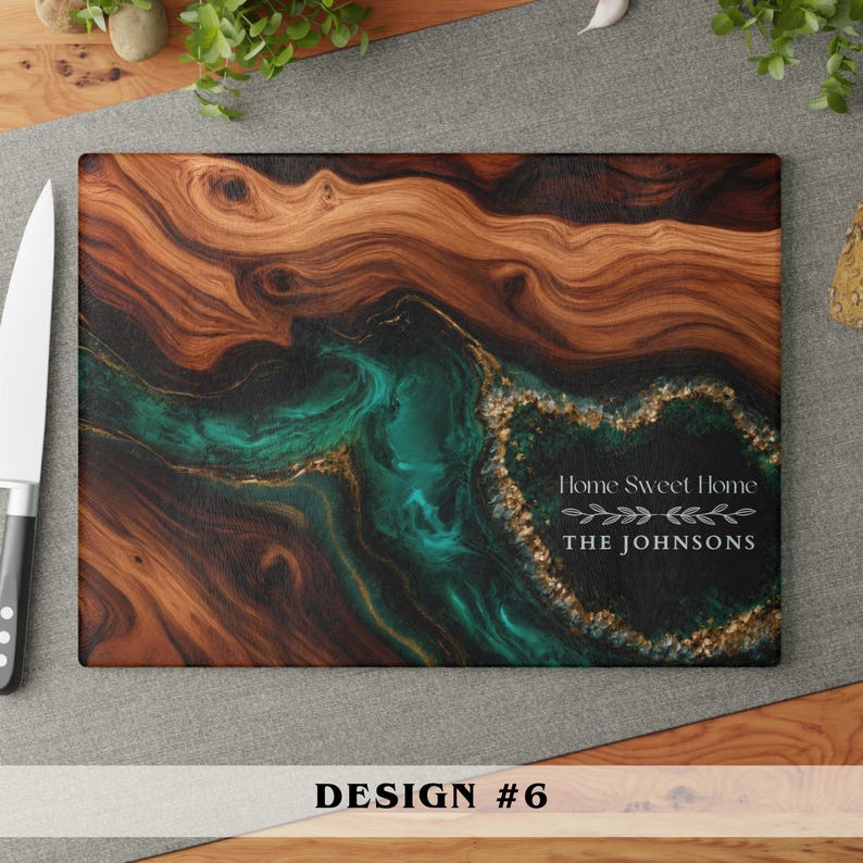 May include: A rectangular cutting board featuring a natural wood grain pattern on the left and a swirling teal and black resin river design on the right. The resin section includes gold flakes and the white text Home Sweet Home THE JOHNSONS.