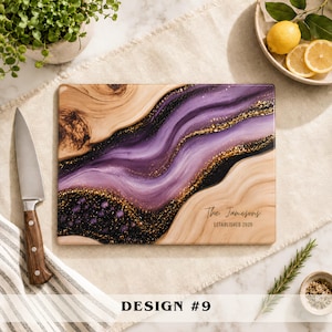 May include: A rectangular wooden cutting board featuring a decorative resin inlay with swirling shades of purple, black, and gold glitter. The board is personalized with the text "The Jamesons" and "ESTABLISHED 2026" printed in black ink.