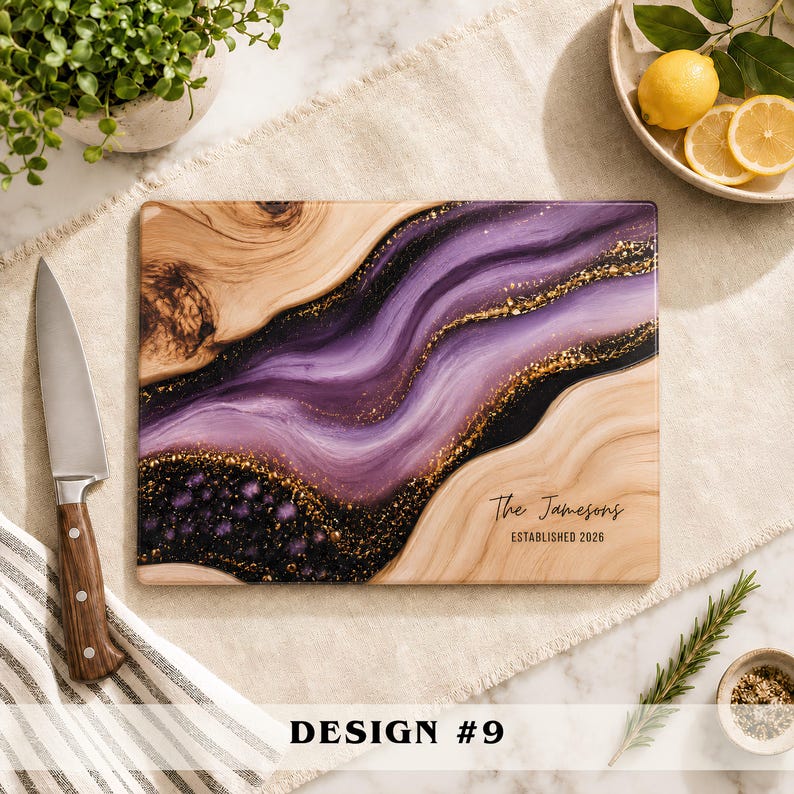 May include: A rectangular wooden cutting board featuring a decorative resin inlay with swirling shades of purple, black, and gold glitter. The board is personalized with the text "The Jamesons" and "ESTABLISHED 2026" printed in black ink.
