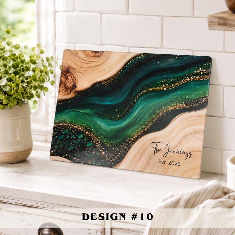 May include: A rectangular wooden serving board featuring a central flowing river design made of dark green and black resin with gold glitter accents. The board is personalized with the black text The Jennings and Est. 2026 on the light wood surface.