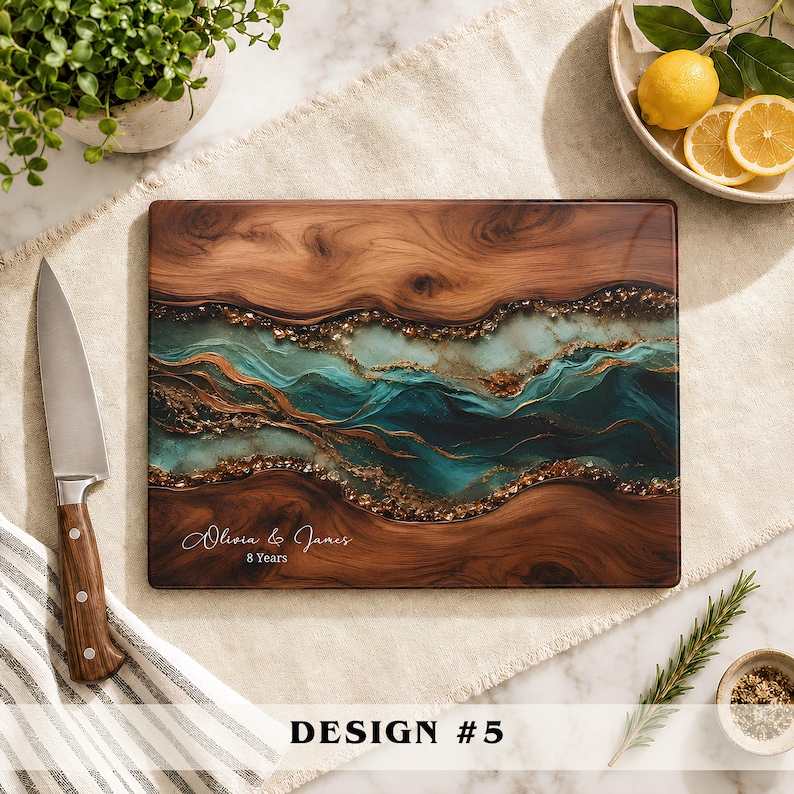 May include: A rectangular wooden cutting board featuring a central resin inlay with swirling teal, blue, and gold metallic accents. The board is engraved with the text Olivia & James 8 Years. A stainless steel knife with a wooden handle sits nearby.