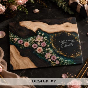 May include: A rectangular wooden serving board featuring a dark resin river inlay filled with pressed pink and white flowers, green foliage, and gold leaf flakes. The board is personalized with the white text KEVIN & IRYNA Elliotts.