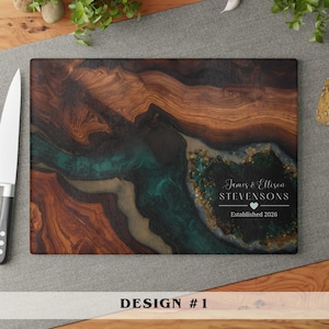 May include: A rectangular wooden cutting board featuring a dark brown wood grain pattern with a swirling teal and gold resin inlay. The board includes white text that reads James & Ellison STEVENSONS, a small heart icon, and Established 2026.
