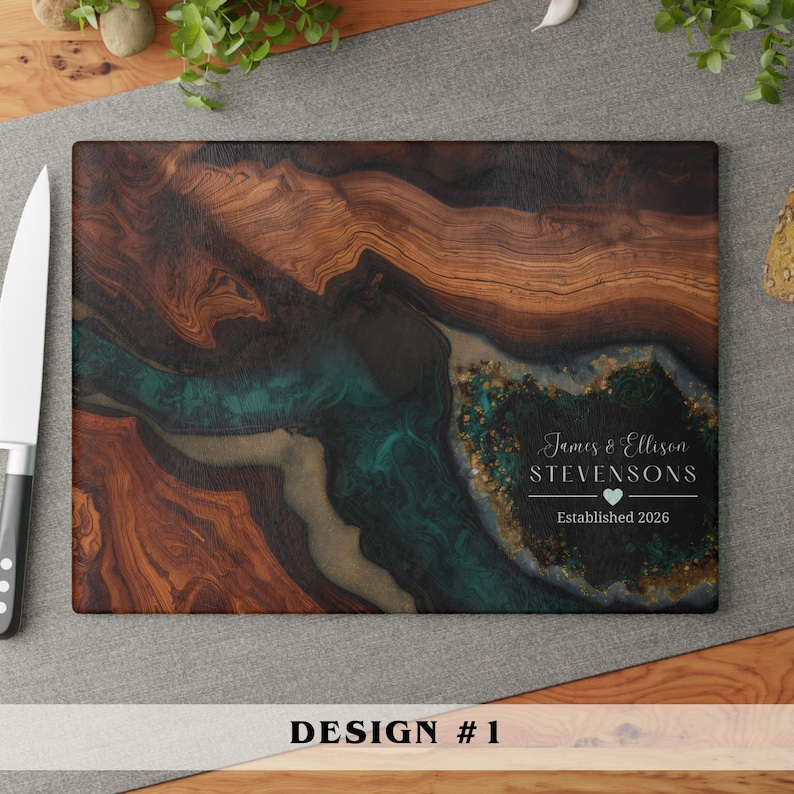 May include: A rectangular wooden cutting board featuring a dark brown wood grain pattern with a swirling teal and gold resin inlay. The board includes white text that reads James & Ellison STEVENSONS, a small heart icon, and Established 2026.