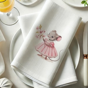 May include: White linen napkin with embroidered image of a mouse wearing a pink dress and holding a bouquet of pink flowers.