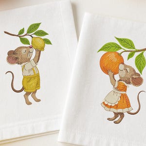 May include: Two white embroidered towels featuring cartoon mice. One mouse is holding a lemon, the other an orange. The mice are wearing yellow overalls and an orange dress. Green leaves and brown branches are also embroidered.