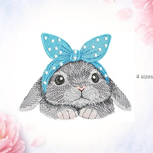 Puede incluir: Diseño bordado de un conejo gris con un lazo azul de lunares. El conejo tiene ojos grandes y oscuros y una nariz rosa. El texto "4 tamaños" es visible.