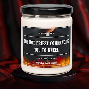 May include: A white candle with a black label that reads "Smells Like The Hot Priest Commanding You To Kneel". The label also includes the text "Scented Candle Flare for the Dramatic Vegan Soy Candle | Cotton Wick | Ethically Sourced and Made in the USA"