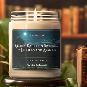 May include: A white candle jar with a silver lid. The label reads "Smells Like Getting Railed in Rivendell by Legolas and Aragorn" and "Scented Candle Flare for the Dramatic Vegan Soy Candle Cotton Wick Ethically Sourced and Made 19.02".