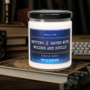 Puede incluir: Una vela perfumada blanca con una etiqueta azul que dice "Smells Like Getting X Rated With Mulder and Scully". La etiqueta también dice "Scented Candle" y "Flare for the Dramatic".