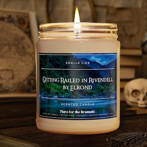 Könnte beinhalten: Eine durchsichtige Glaskerze in einem Glas mit einem weißen Etikett, auf dem "Smells Like Getting Railed in Rivendell by Elrond" steht. Das Etikett trägt außerdem die Aufschrift "Scented Candle Flare for the Dramatic" und "Vegan Soy Candle | Cotton Wick | Ethically Sourced and Made 8 oz".
