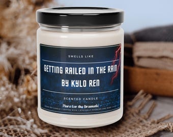 May include: A white soy candle with a black lid and label. The label reads "Smells Like Getting Railed in the Rain by Kylo Ren" and "Scented Candle Flare for the Dramatic".
