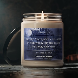 Puede incluir: Un tarro de vela de vidrio marrón con una etiqueta blanca. La etiqueta tiene una ilustración azul y blanca de un barco pirata y el texto "Smells Like Getting Your Booty Pillaged At The Prow Of The Pearl By Jack And Will". La etiqueta también dice "Vela perfumada Flare for the Dramatic Vela de soja vegana | Mecha de algodón | De origen ético y fabricación"