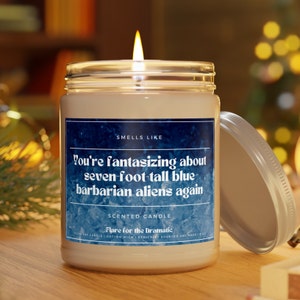 May include: A white scented candle in a clear glass jar with a blue label that reads "You're fantasizing about seven-foot-tall blue barbarian aliens again". The label also says "Smells Like" and "Scented Candle".