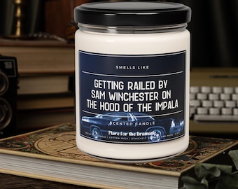 May include: A white candle with a black lid and a label that reads "Smells Like Getting Railed By Sam Winchester On The Hood Of The Impala" with a blue and black image of a car. The label also says "Scented Candle" and "Flare for the Dramatic".