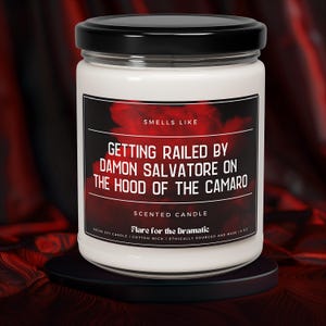May include: White candle jar with a black lid and a red and black label that reads "Smells Like Getting Railed By Damon Salvatore On The Hood Of The Camaro" and "Scented Candle". The label also includes the text "Flare for the Dramatic", "Vegan Soy Candle", "Cotton Wick", and "Ethically Sourced and Made 18 oz".