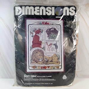 Peut inclure: Un kit de broderie crewel Dimensions intitulé Aesop's Fables conçu par Linda K. Powell. L'emballage présente un motif imprimé de renard, tortue, souris et lion. Il inclut une taille de cadre de 51 cm sur 51 cm et du fil de laine persane.