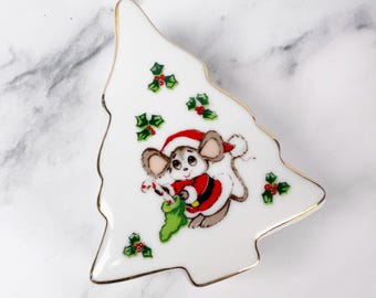 May include: White ceramic Christmas tree-shaped plate with a gold rim. The plate features a cartoon mouse dressed as Santa Claus, holding a stocking and candy cane. Holly and berry accents are scattered across the plate.