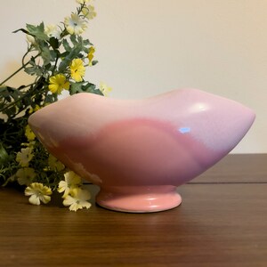 May include: A pink ceramic planter with a unique, wavy design. The planter has a wide, shallow bowl shape with a raised base.
