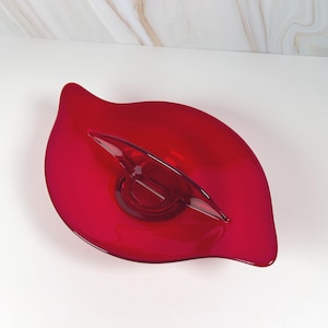 May include: A vibrant red glass serving dish with a unique leaf shape. The dish features a central, clear glass accent and is designed with smooth, flowing lines. This decorative piece is ideal for serving snacks or as a centerpiece.