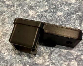 May include: A black, rectangular trailer hitch receiver with a square opening and a connecting piece. The receiver has a hole for a pin and is made of a durable material.