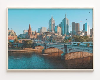 Könnte beinhalten: Ein gerahmtes Foto einer Stadtlandschaft mit einer Brücke über einem Fluss. Die Skyline der Stadt zeigt hohe Gebäude, darunter einen Kirchturm, und eine Brücke mit Steinbögen. Der Fluss ist blau und ruhig, mit ein paar Booten in der Ferne. Der Himmel ist hellblau mit ein paar weißen Wolken.