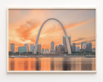 Op de afbeelding: Een panoramisch uitzicht op de St. Louis Gateway Arch met de skyline van de stad op de achtergrond. De boog is een belangrijk monument in St. Louis, Missouri, en is een populaire toeristische bestemming. De lucht is een levendig oranje en roze, wat een prachtige zonsondergang achtergrond creëert.